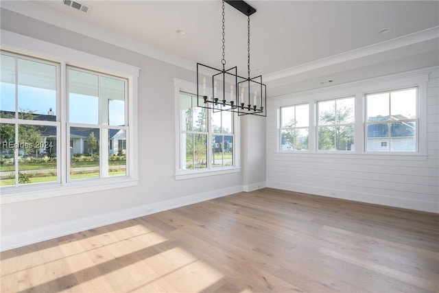 unfurnished dining area with a healthy amount of sunlight, ornamental molding, wood-type flooring, and a chandelier