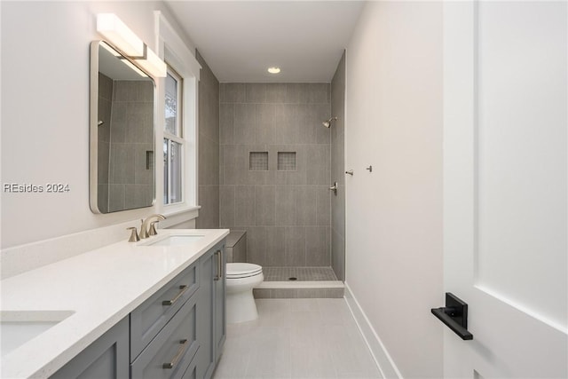 bathroom with tiled shower, vanity, toilet, and tile patterned flooring