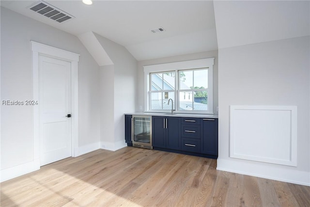 bar with blue cabinetry, sink, vaulted ceiling, beverage cooler, and light hardwood / wood-style floors