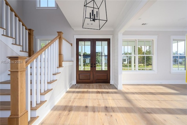 entrance foyer with an inviting chandelier, crown molding, light hardwood / wood-style flooring, and french doors