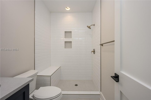 bathroom with tile patterned flooring, vanity, a tile shower, and toilet