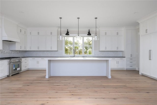 kitchen featuring premium range hood, stainless steel range, decorative light fixtures, and light hardwood / wood-style floors