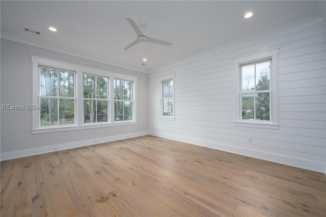 empty room featuring a wealth of natural light, ornamental molding, wood walls, and light wood-type flooring