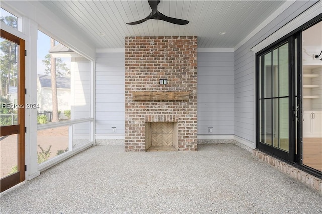 unfurnished sunroom featuring a brick fireplace, wooden ceiling, and ceiling fan