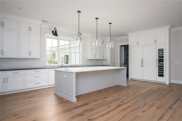 kitchen featuring light wood-type flooring, hanging light fixtures, a kitchen island, and white cabinets