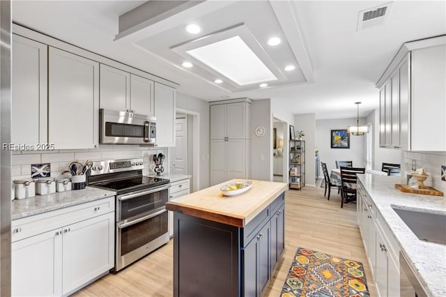 kitchen with white cabinetry, wood counters, stainless steel appliances, and backsplash