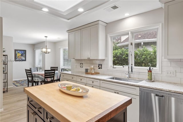 kitchen featuring light stone countertops, decorative light fixtures, light hardwood / wood-style flooring, and stainless steel dishwasher