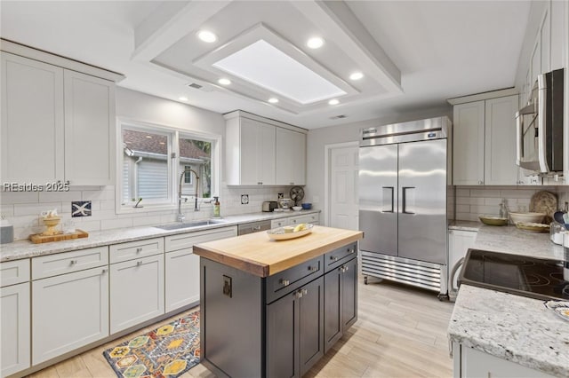 kitchen featuring appliances with stainless steel finishes, butcher block countertops, a skylight, sink, and a center island