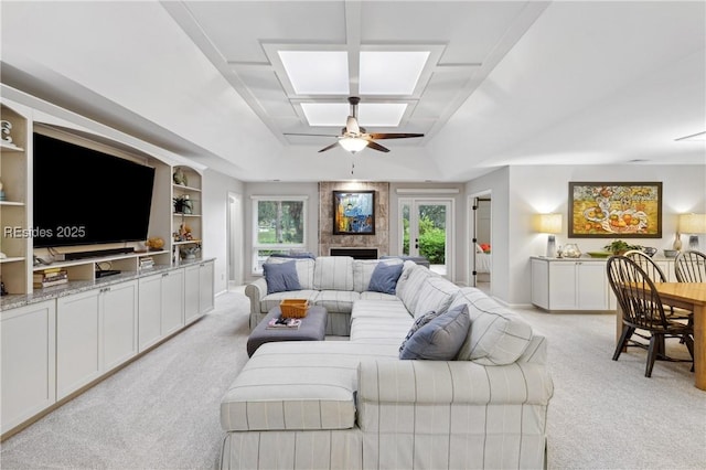 living room featuring built in shelves, light carpet, ceiling fan, and a tray ceiling