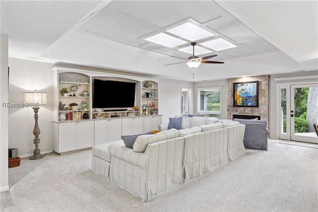 carpeted living room with a tile fireplace, ceiling fan, a skylight, a tray ceiling, and built in shelves