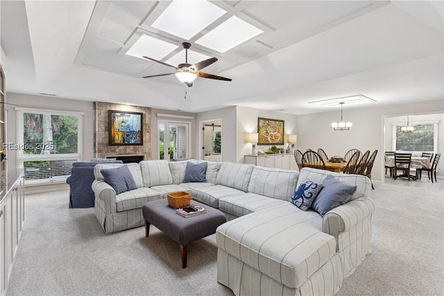 carpeted living room with a tiled fireplace, ceiling fan with notable chandelier, plenty of natural light, and a raised ceiling