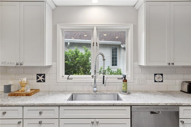 kitchen with sink, tasteful backsplash, light stone countertops, white cabinets, and stainless steel dishwasher