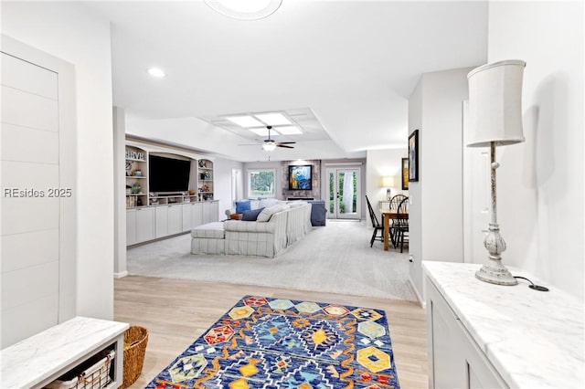 living room with light hardwood / wood-style flooring, built in features, a raised ceiling, and ceiling fan