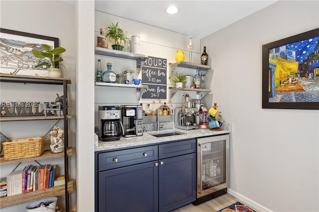 bar featuring wine cooler, blue cabinets, sink, light wood-type flooring, and light stone countertops