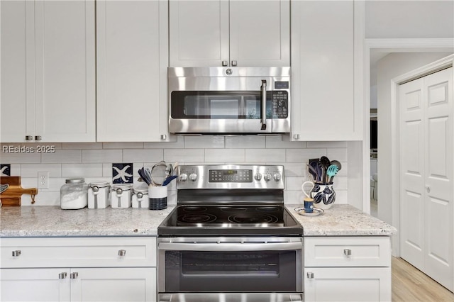 kitchen with light stone counters, backsplash, stainless steel appliances, and white cabinets