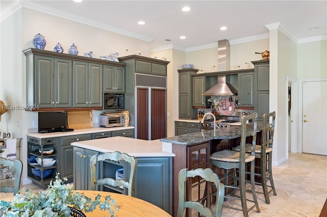 kitchen featuring a kitchen island with sink, stove, range hood, ornamental molding, and paneled fridge