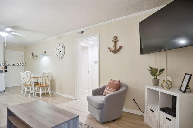 living room featuring ornamental molding, wooden walls, ceiling fan, and light hardwood / wood-style floors