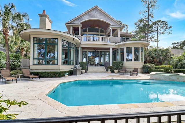 back of property featuring a balcony, a swimming pool with hot tub, ceiling fan, a sunroom, and a patio area