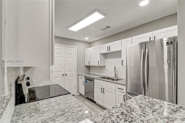 kitchen with appliances with stainless steel finishes, sink, white cabinets, and light stone counters