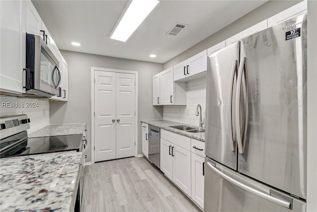 kitchen with light stone counters, appliances with stainless steel finishes, sink, and white cabinets