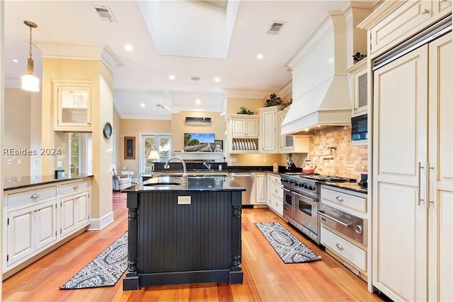 kitchen with high quality appliances, custom range hood, pendant lighting, and light hardwood / wood-style floors