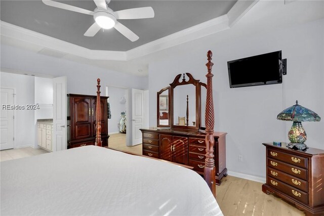 bedroom with light hardwood / wood-style floors, connected bathroom, ceiling fan, and a tray ceiling