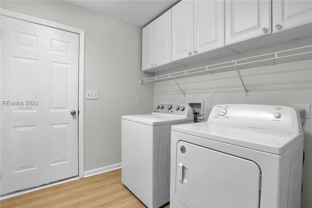 clothes washing area featuring light hardwood / wood-style flooring, washer and clothes dryer, and cabinets