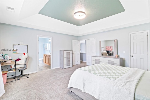 bedroom featuring light carpet, a raised ceiling, a textured ceiling, and ensuite bathroom