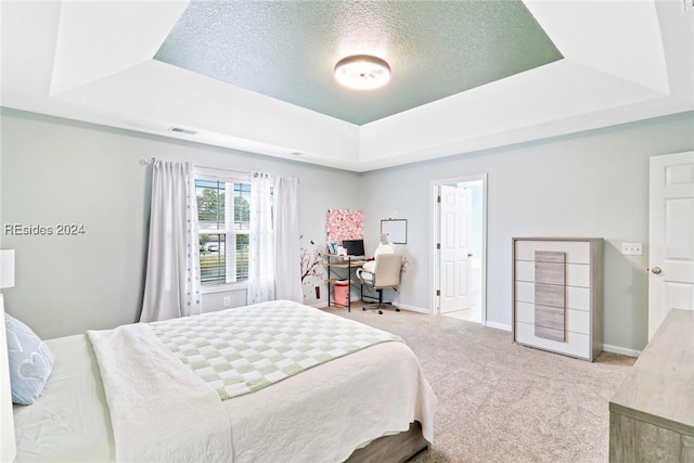 bedroom with a tray ceiling, light colored carpet, and a textured ceiling