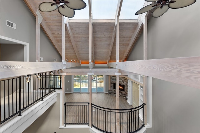 stairs featuring wood ceiling, ceiling fan, a stone fireplace, and lofted ceiling with beams