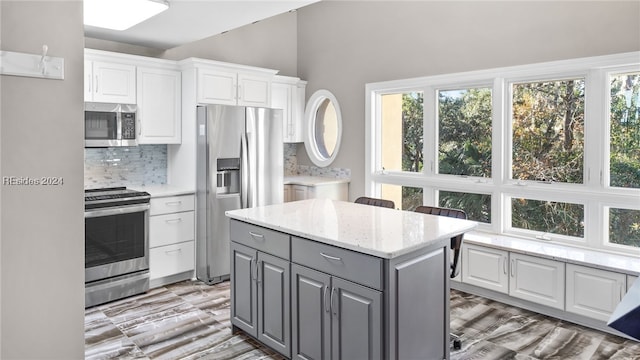 kitchen featuring appliances with stainless steel finishes, tasteful backsplash, white cabinetry, gray cabinetry, and a center island