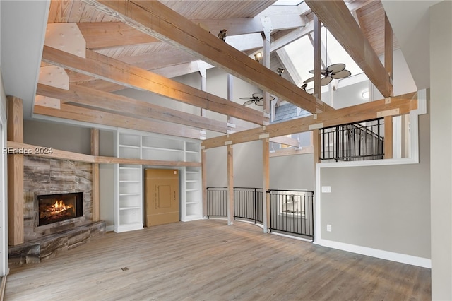 unfurnished living room with beam ceiling, a stone fireplace, built in features, and ceiling fan