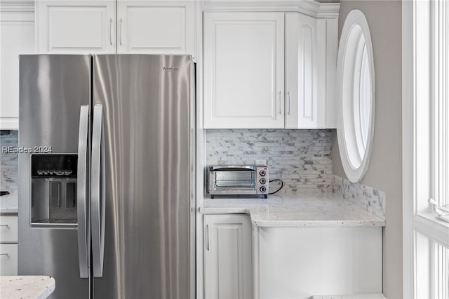 kitchen featuring stainless steel refrigerator with ice dispenser, decorative backsplash, light stone counters, and white cabinets