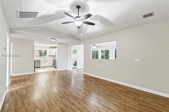 unfurnished living room with vaulted ceiling, ceiling fan, a textured ceiling, and light wood-type flooring