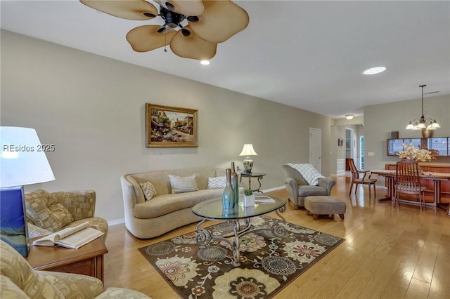 living room featuring ceiling fan with notable chandelier and light hardwood / wood-style floors