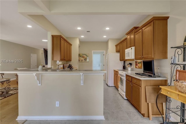 kitchen featuring light tile patterned flooring, white appliances, kitchen peninsula, and a breakfast bar area