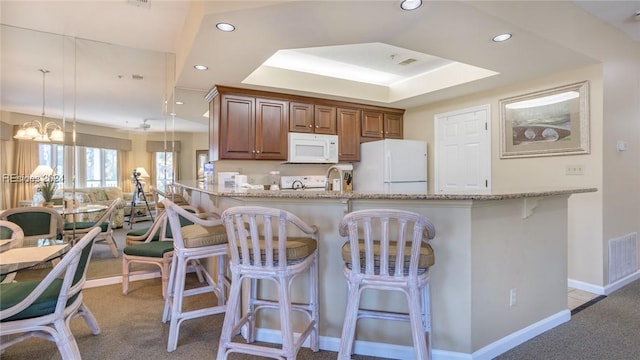 kitchen with hanging light fixtures, kitchen peninsula, light stone countertops, light carpet, and white appliances