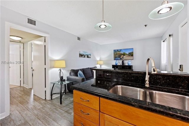 kitchen featuring hanging light fixtures, sink, light hardwood / wood-style floors, and dark stone counters