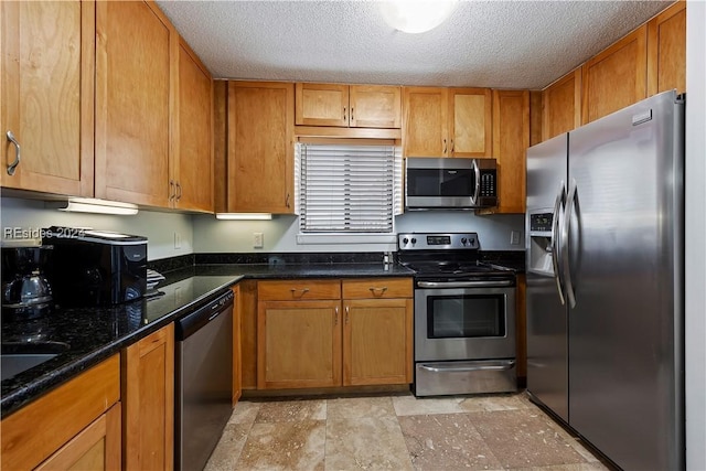 kitchen with stainless steel appliances, dark stone countertops, and a textured ceiling