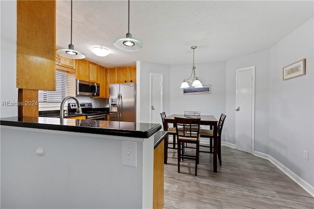 kitchen with decorative light fixtures, a textured ceiling, appliances with stainless steel finishes, kitchen peninsula, and hardwood / wood-style flooring