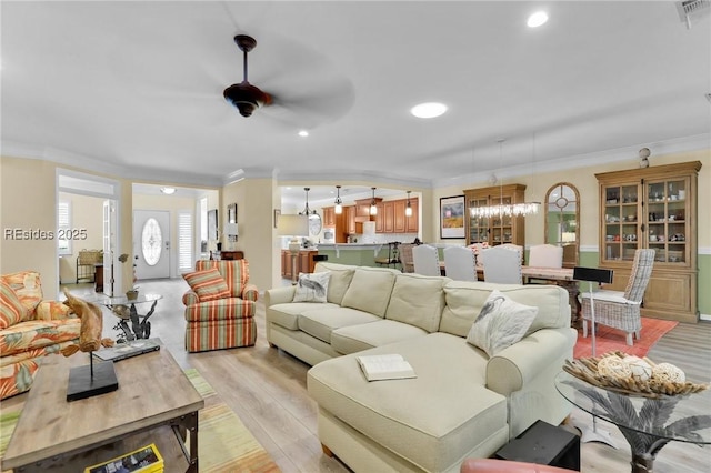 living room with ornamental molding, ceiling fan with notable chandelier, and light hardwood / wood-style floors