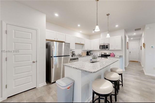 kitchen with white cabinetry, a center island, appliances with stainless steel finishes, a kitchen breakfast bar, and light stone countertops