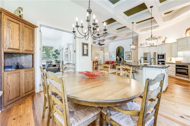 dining space featuring light hardwood / wood-style flooring, beam ceiling, a high ceiling, coffered ceiling, and ceiling fan with notable chandelier