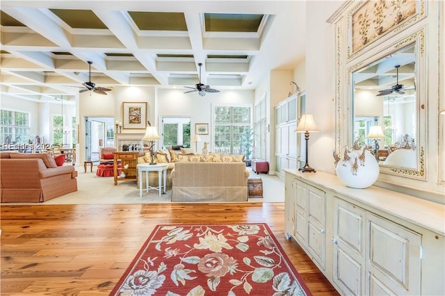 living room with light hardwood / wood-style flooring, beam ceiling, a wealth of natural light, and coffered ceiling