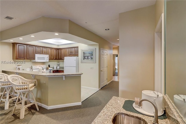 kitchen featuring sink, white appliances, a kitchen breakfast bar, light stone counters, and kitchen peninsula