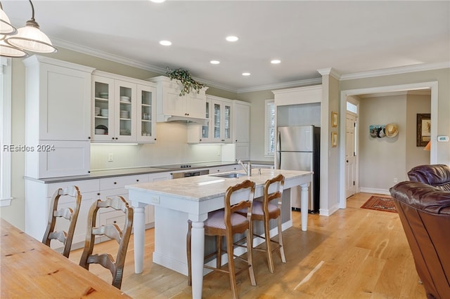 kitchen featuring pendant lighting, sink, stainless steel fridge, white cabinets, and a center island with sink