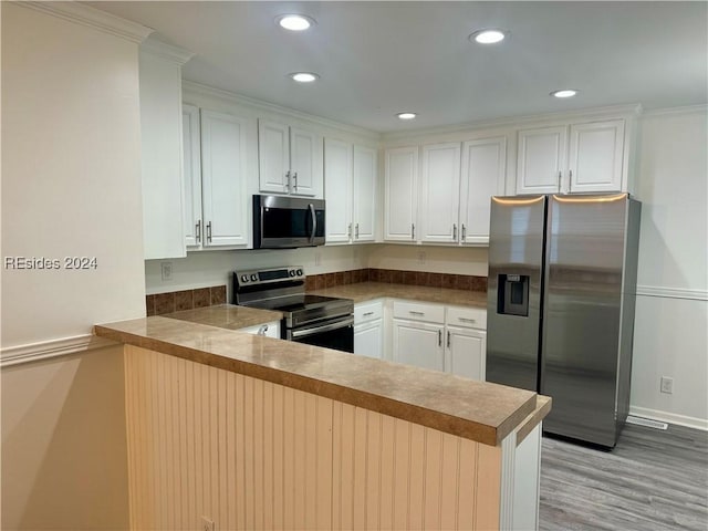 kitchen featuring white cabinets, ornamental molding, kitchen peninsula, stainless steel appliances, and light hardwood / wood-style flooring