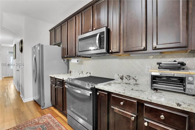 kitchen with tasteful backsplash, light hardwood / wood-style floors, stainless steel appliances, light stone countertops, and dark brown cabinets