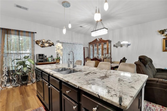 kitchen with pendant lighting, dishwasher, an island with sink, sink, and light hardwood / wood-style flooring