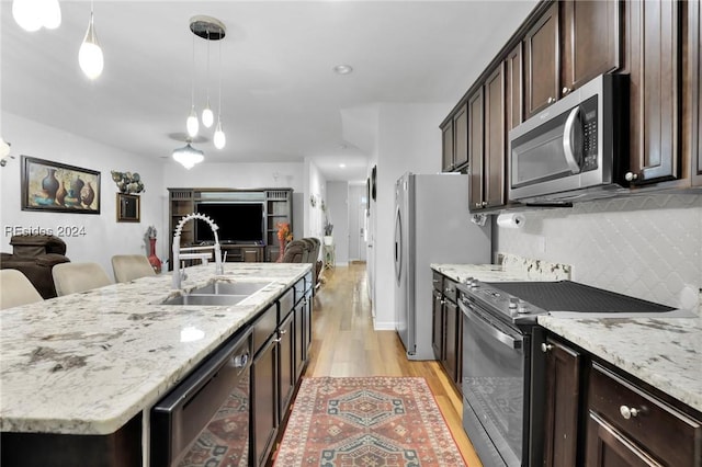 kitchen with sink, a kitchen island with sink, hanging light fixtures, stainless steel appliances, and decorative backsplash